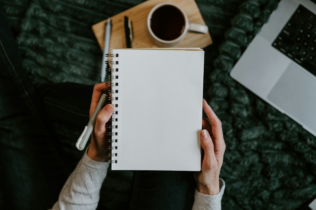 Hands holding a blank notebook with coffee and laptop