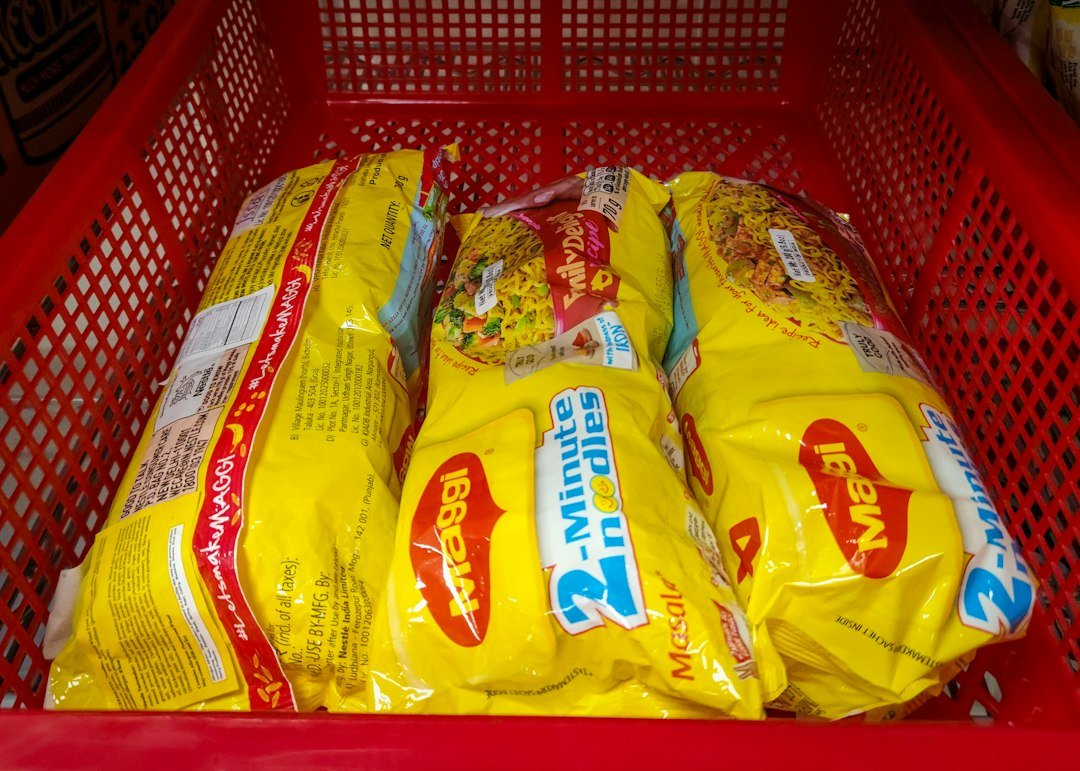 Three yellow packages of instant noodles inside a red plastic crate